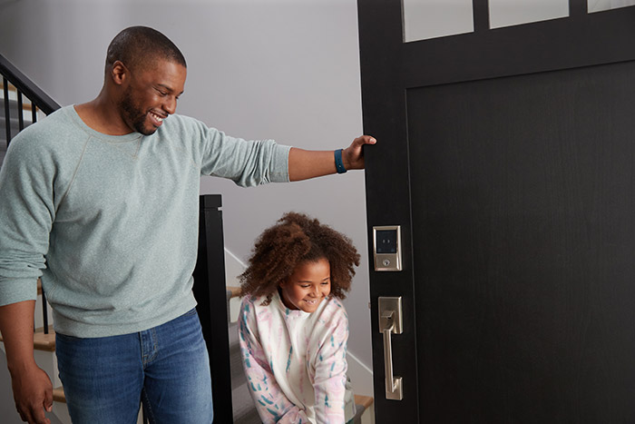 Father holding front door open for daughter with Schlage Encode Plus homekit smart lock.